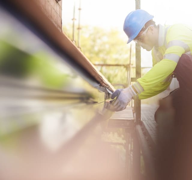 Man in safety jacket, hard hat and gloves measuring building